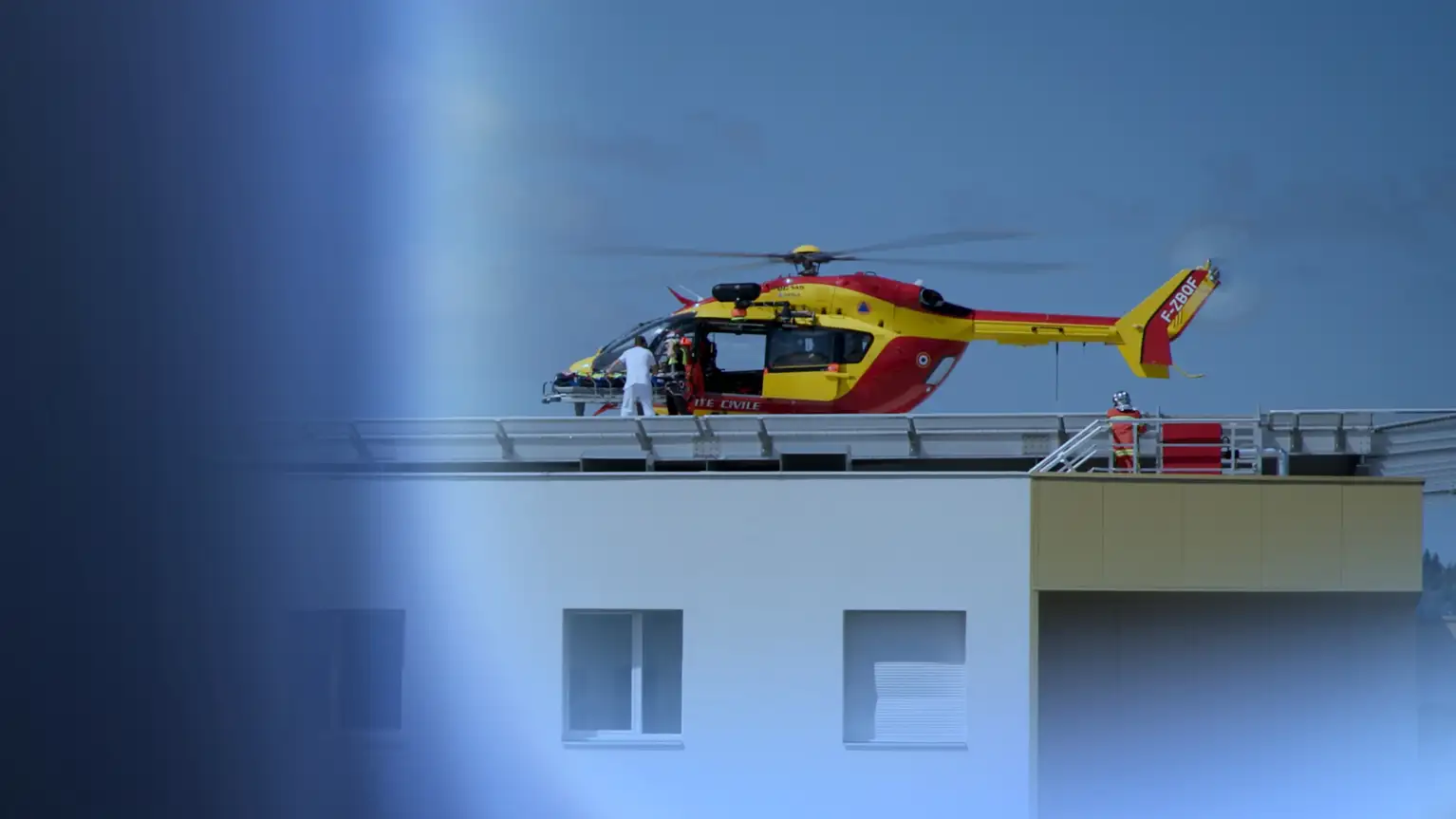 Medical helicopter on hospital rooftop with paramedics loading a patient on a stretcher.