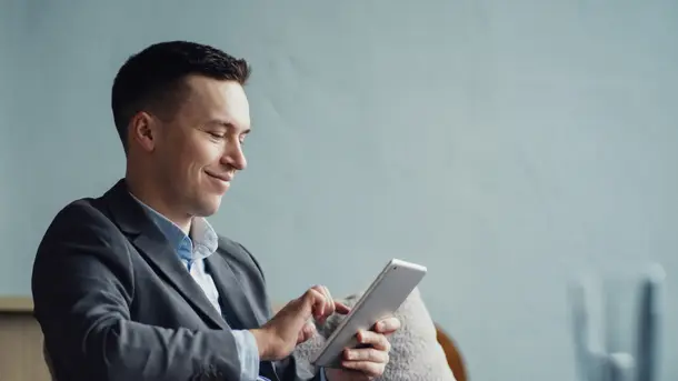 Man in a business suit using a tablet while sitting on a couch.