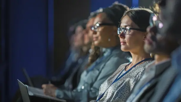 Audience members sitting in a row attentively watching a presentation at a conference.