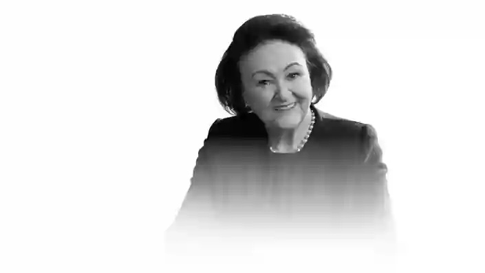 Woman wearing a blazer and pearl necklace sitting with hands folded, monochrome style.