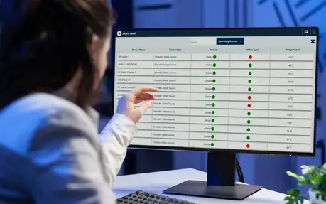 Person interacting with a computer monitor displaying a device health status dashboard.