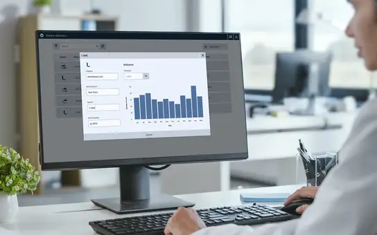 Person using a computer to view medical device utilization data and bar chart on a monitor.