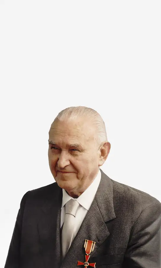 Older man in a suit with a white tie and a medal pinned to his jacket.