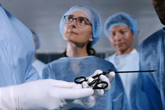 Surgeon handing laparoscopic surgical instrument to a medical professional in an operating room.