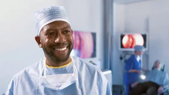 Smiling surgeon wearing surgical cap and mask around neck in a medical setting.
