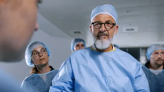 Medical team wearing surgical gowns and caps, with a senior doctor in focus.