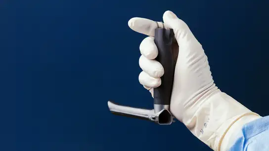 Gloved hand holding a laryngoscope for medical examination.