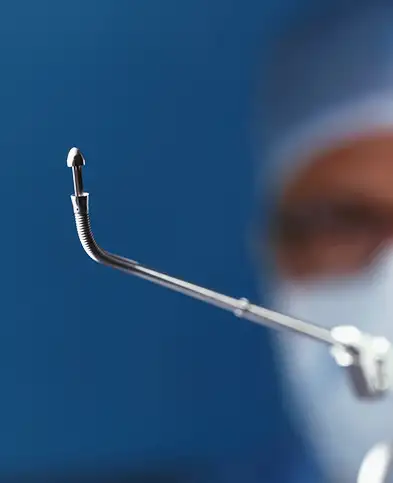 A surgical instrument held by a medical professional wearing a mask.