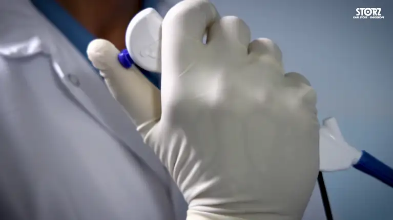 Gloved hand holding a medical endoscope control device.