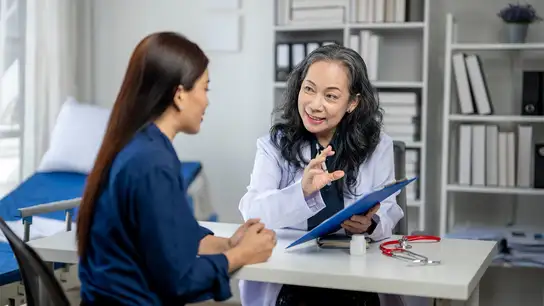 Female doctor consulting with a patient, holding a clipboard and explaining medical information.