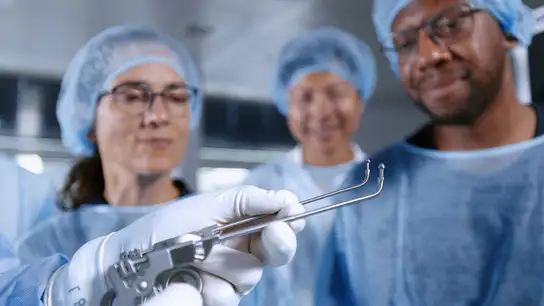 Surgeons examine medical instruments during an operation in a sterile environment.