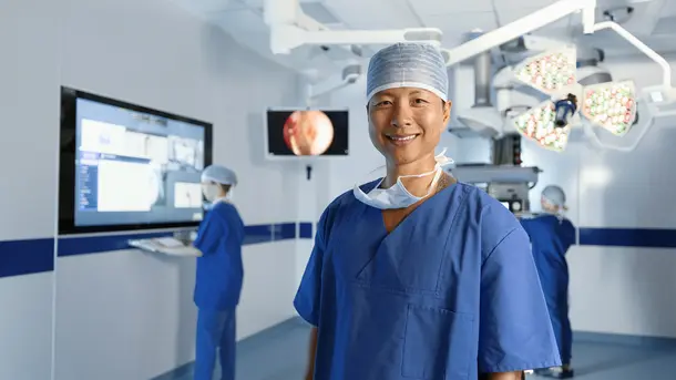 Smiling surgeon wearing blue scrubs and a cap in a modern operating room.